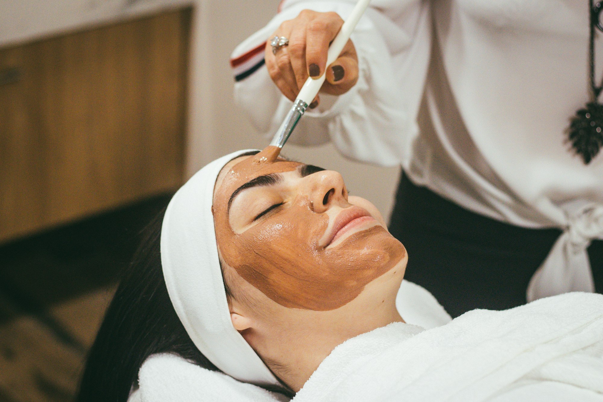 Client in a white robe relaxing during a face mask treatment